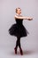 Young blonde ballerina girl dance and posing in black tutu and ballet shoes on grey background