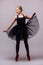 Young blonde ballerina girl dance and posing in black tutu and ballet shoes on grey background.