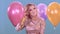 A young blonde in a beautiful dress against the background of balloons rejoices at her holiday, birthday.