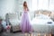 A young blonde bride in a magnificent purple dress is in the bedroom. In the room candles and bouquets of flowers.