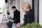 Young blonde in dark coat and young guy in coat sit on street in downtown near cafe and look at tablets