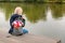 Young blonde dreamy woman with bouquet of flowers in grey backpack near a river.