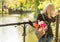 Young blonde dreamy woman with bouquet of flowers in grey backpack in a spring summer park