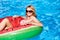 Young blonde girl having fun and laughing on an inflatable watermelon pool swim ring in bikini. Attractive woman in