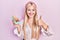 Young blonde girl holding delicious macarons pastries smiling happy and positive, thumb up doing excellent and approval sign