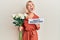 Young blonde girl holding flowers and paper with happy valentines message angry and mad screaming frustrated and furious, shouting
