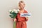 Young blonde girl holding flowers and paper with happy valentines message angry and mad screaming frustrated and furious, shouting