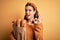 Young blonde girl holding supermarket paper bag full of fresh bread over yellow background doing ok sign with fingers, excellent