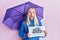 Young blonde girl holding umbrella rain draw afraid and shocked with surprise and amazed expression, fear and excited face