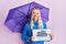 Young blonde girl holding umbrella rain draw sticking tongue out happy with funny expression