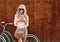 Young blonde girl with long hair with brown vintage bag in sunglasses standing near vintage green bicycle and holding a cup o