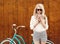 Young blonde girl with long hair in sunglasses standing near vintage green bicycle and holding a cup of coffee have fun and g
