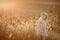 Young blonde girl playing with sunlight in the fields sunset wearing a dress with hill in the background