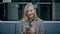 Young blonde girl sitting in modern metro, looking at her phone and smiling