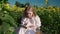 A young blonde girl in a sunflower field reads a book, looks around, waits