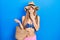 Young blonde girl wearing bikini and hat holding summer wicker handbag covering mouth with hand, shocked and afraid for mistake