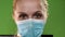 Young blonde girl wearing medical mask at green screen.