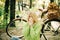 Young blonde in a green sweater sitting on the ground in the park blowing her nose on bicycle background. Seasonal