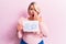 Young blonde plus size woman asking for positive change holding paper with emotion message covering mouth with hand, shocked and