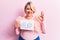Young blonde plus size woman asking for positive change holding paper with emotion message doing ok sign with fingers, smiling