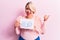 Young blonde plus size woman asking for positive change holding paper with emotion message pointing thumb up to the side smiling