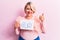 Young blonde plus size woman asking for positive change holding paper with emotion message smiling happy and positive, thumb up