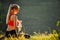 A young blonde in a red top and black pants sits on the grass in nature. A sporty woman is holding a bottle of water.