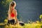 A young blonde in a red top sits on the grass for fitness in nature. A sportswoman prepares for gymnastics.