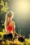 A young blonde in a red top sits on the grass for fitness in nature. A sportswoman prepares for gymnastics.