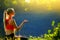 A young blonde in a red top sits on the grass in nature. A sporty woman throws holds a green apple in her hands