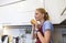 young blonde sniffs a broken baguette, holds it in her hands by the nose in kitchen