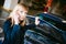Young blonde stands near car with raised engine compartment hood
