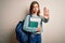 Young blonde student girl wearing backpack and books from school over isolated background with open hand doing stop sign with