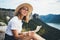 Young blonde tourist holds in hands map of  landscape and looks views top of mountain, cute smiling girl in hat and glasses leisur