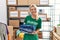 Young blonde volunteer girl smiling happy holding stack of folded jeans at charity center