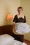 Young blonde woman 39 years old in the uniform of a hotel maid. Next to a large double bed. Change bed linen and bedding