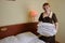 Young blonde woman 39 years old in the uniform of a hotel maid. Next to a large double bed. Change bed linen and bedding