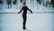 Young blonde woman in black clothes with high ponytail figure skating on the public ice rink in the morning