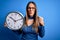 Young blonde woman with blue eyes holding big minute clock over isolated background annoyed and frustrated shouting with anger,