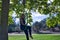 Young blonde woman in a blue suit, sitting on an aero hoop hanging from a tree in the middle of a park. Concept aerial hoop, pole