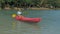 Young blonde woman in blue swimsuit rows pink plastic canoe along azure sea bay past island with palms under blue sky at