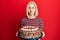 Young blonde woman celebrating birthday holding big chocolate cake puffing cheeks with funny face