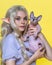 Young blonde woman cosplay elf in blue dress holding Sphinx kitten in hands and showing it