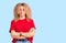 Young blonde woman with curly hair wearing casual red tshirt skeptic and nervous, disapproving expression on face with crossed