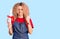 Young blonde woman with curly hair wearing hairdresser apron and holding diploma annoyed and frustrated shouting with anger,