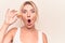 Young blonde woman eating french dessert holding chocolate macaron over white background scared and amazed with open mouth for