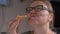 Young blonde woman with glasses greedily bites off a slice of spicy pepperoni pizza and chews with pleasure, close up