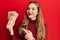 Young blonde woman holding 5000 hungarian forint banknotes smiling happy pointing with hand and finger