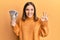 Young blonde woman holding 5000 japanese yen banknotes covering mouth with hand, shocked and afraid for mistake