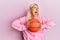 Young blonde woman holding basketball ball angry and mad screaming frustrated and furious, shouting with anger